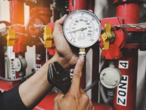 Technician checking fire sprinkler system water pressure gauge during NFPA 25 inspection and testing in a commercial building.